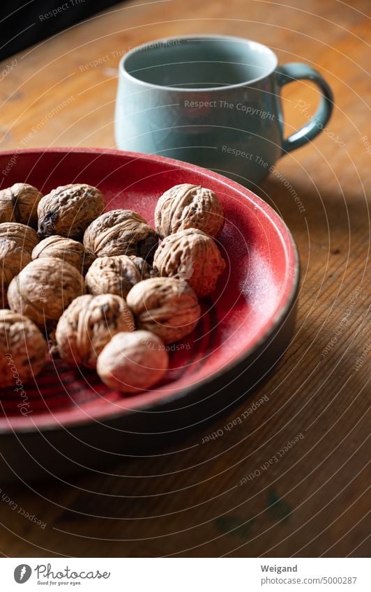 Walnüsse in einer roten Keramikschale auf einem Holztisch mit einer hellblauen Tasse im Hintegrund Walnuss Nüsse Tonschale rote Schale Tasse mit Henkel mint