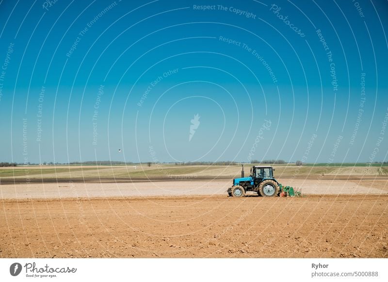 Traktor Pflügen Feld im Frühjahr Saison. Beginn der landwirtschaftlichen Frühjahrssaison. Cultivator Pulled By A Tractor In Countryside Rural Field Landscape Under Clear Sunny Spring Blue Sky. Skyline