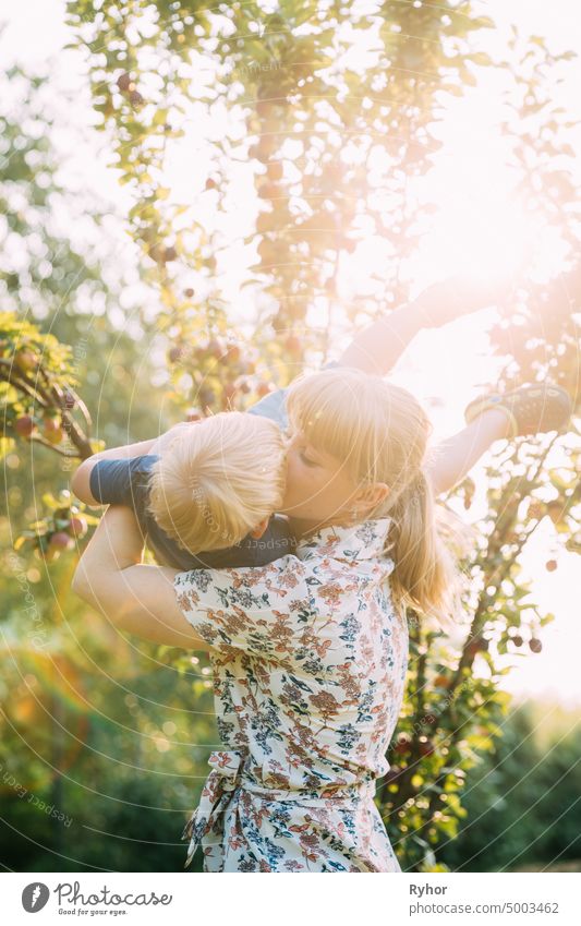 Junge Frau Mutter umarmt und küsst ihr Baby Sohn im sonnigen Garten. Outdoor Sommer Porträt schön blond Pflege Kaukasier Kind Kindheit filigran Kleid Abend