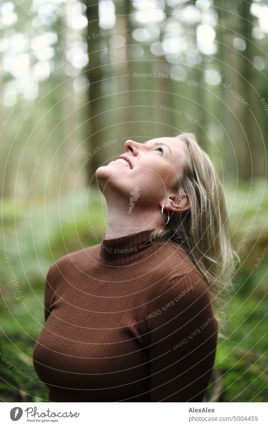 Junge, blonde Frau mit Grübchen steht im Wald und schaut lächelnd nach oben zum Himmel junge Frau feminin schön glücklich Jugendliche Portrait Erwachsene