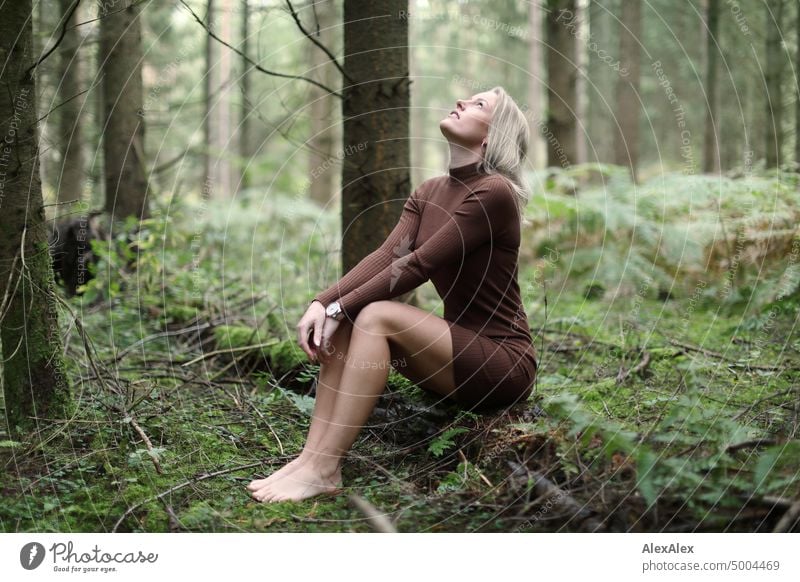 Junge, blonde Frau sitzt barfuß auf einem umgefallenen Baumstamm im Wald und schaut in den Himmel junge Frau feminin schön glücklich Jugendliche Portrait