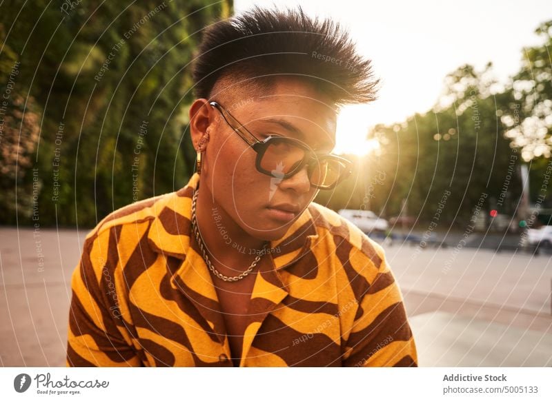 Trendiger Mann mit Sonnenbrille bei Sonnenuntergang in der Stadt nicht binär trendy urban cool Streetstyle lgbtq Großstadt Abenddämmerung Sonnenlicht Ohrringe