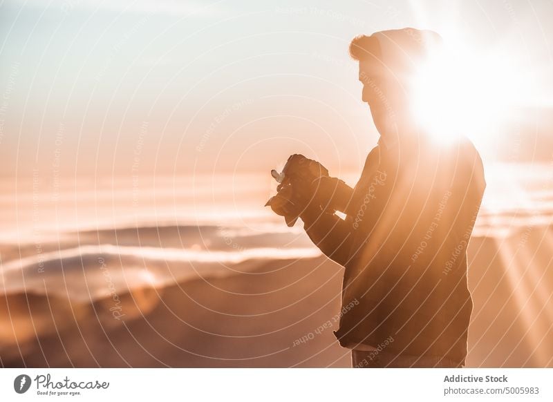 Silhouette eines Mannes im Gegenlicht beim Betrachten von Fotos in seiner Spiegelreflexkamera Fotograf Landschaft Fotokamera Person Abend Licht Himmel reisen