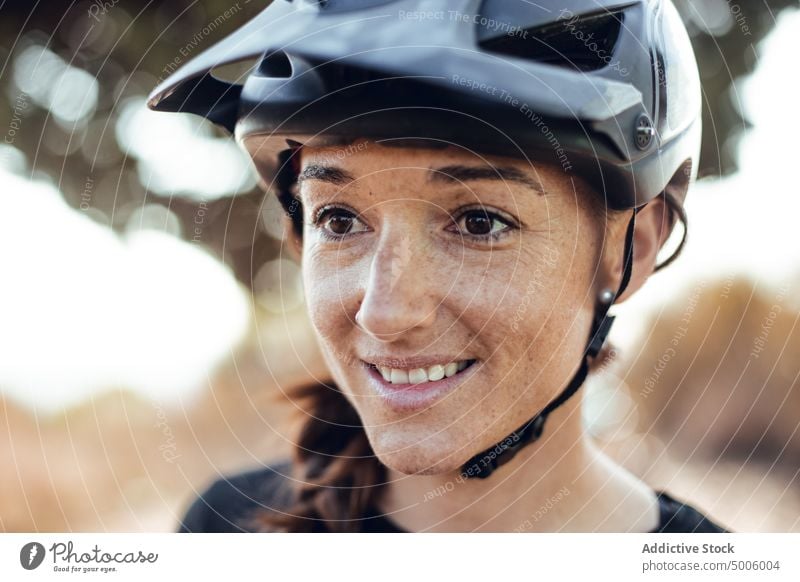 Frau knöpft Helm und Fahrrad in der Nähe eines Baumes zu Schutzhelm knöpfend Sport extrem Lächeln Aktivität Handschuhe Sicherheit Wald jung Dame attraktiv