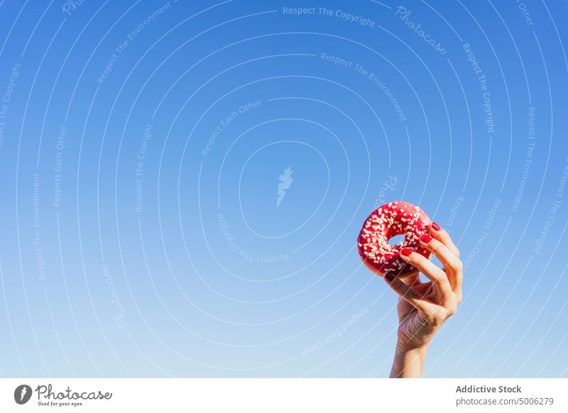 Frau mit rosa Donut an einem Sommertag Krapfen Hand Blauer Himmel farbenfroh süß geschmackvoll Lebensmittel Dessert lecker bestäuben Leckerbissen Gebäck zeigen