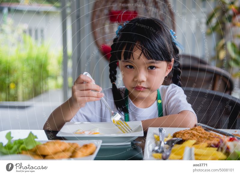 kleines Mädchen asiatischen essen Spiegelei auf Teller am Tisch. wenig Ei gebraten Kind Person Gabel jung Morgen Baby heimwärts Lächeln Küche weiß genießen