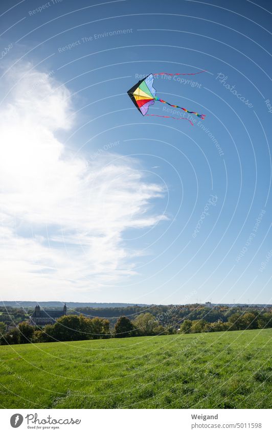 Ein bunter Drache steigt vor blauem Himmel mit weißen Wolken über der Comburg in Schwäbisch Hall auf und fliegt über grüne Wiesen Berg Drachensteigen