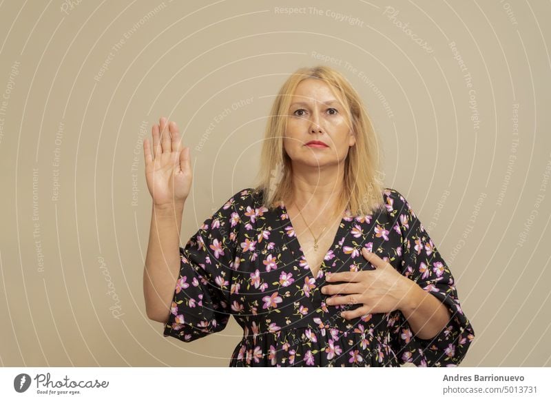 Schöne elegante kaukasische Frau auf einem beigen isolierten Hintergrund. Schwören mit der Hand auf der Brust und den Fingern, wobei ein Treuegelöbnis Eid.