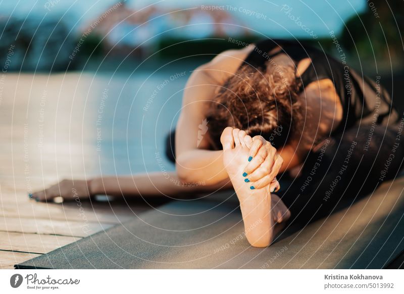 Dehnender Fuß in Nahaufnahme. Mädchen macht Split Twine. Hanumanasana, Affenhaltung. Junge orientalische Aussehen Frau übt Yoga auf Holzdeck in tropischen Insel