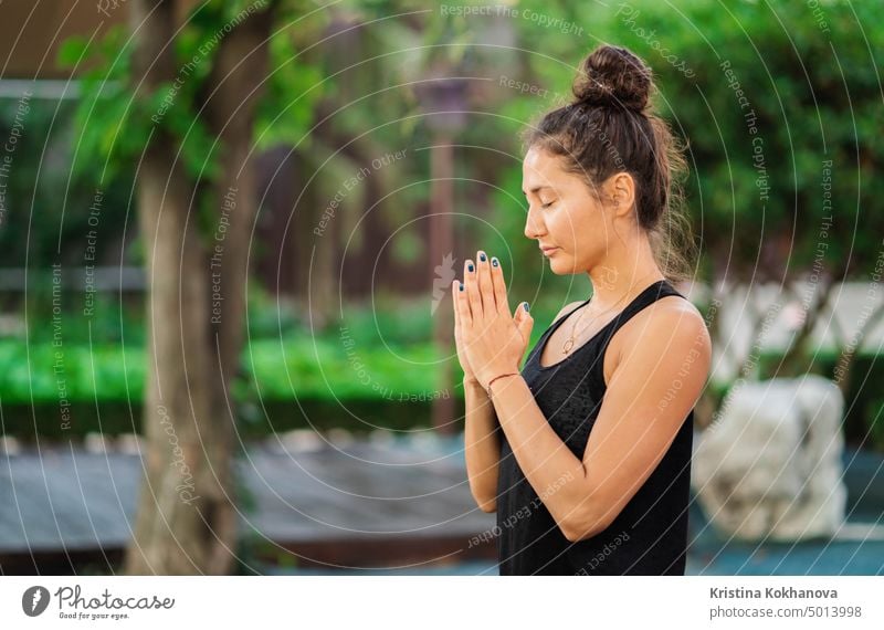 Konzentriertes Mädchen sitzt im Lotussitz mit Händen in Namaste und meditiert oder betet. Junge Frau mit orientalischem Aussehen übt Yoga allein auf einem Holzdeck auf einer tropischen Insel.