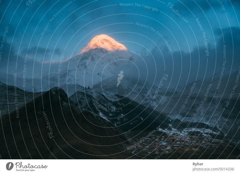 Stepantsminda, Georgien. Mount Kazbek in Morning Sunlit und berühmte Gergeti Kirche bei Sonnenaufgang. Erstaunlich schöne georgische Landschaft im frühen Winter