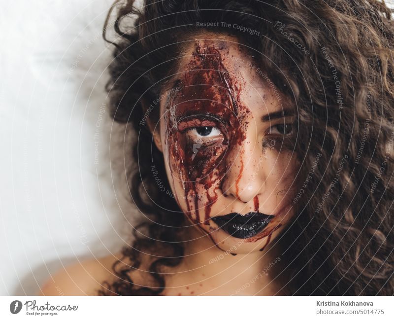 Scary Porträt der jungen Zombie-Frau mit Halloween Blut Make-up. Schönes lateinisch geschlagenes Mädchen mit lockigem Haar schaut in die Kamera. Erwachsener