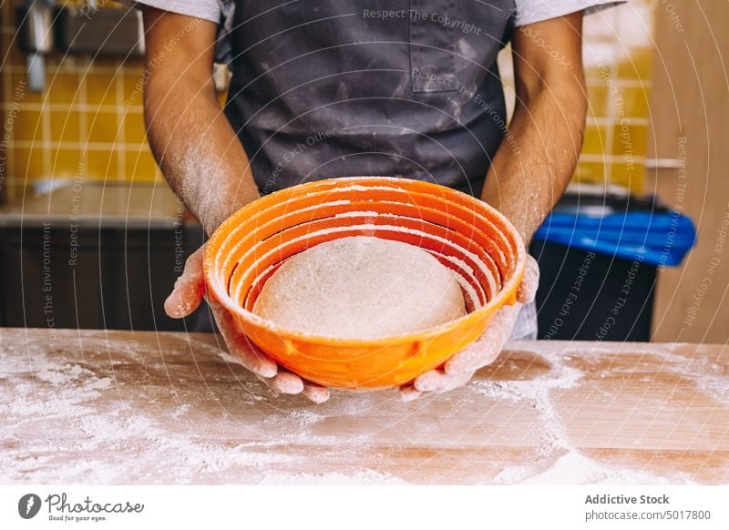 Männlicher Bäcker mit Teig im Gärkorb Teigwaren roh Mann Brot Bäckerei Küche vorbereiten Prozess männlich frisch Küchenchef Koch Schürze kulinarisch Tisch