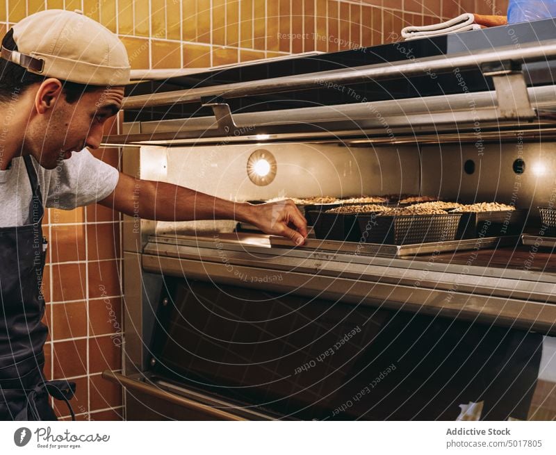 Mann beim Brotbacken im Backofen Bäckerei Ofen Koch Küche Teigwaren industriell männlich Tablett Schürze Gebäck vorbereiten Lebensmittel frisch kulinarisch