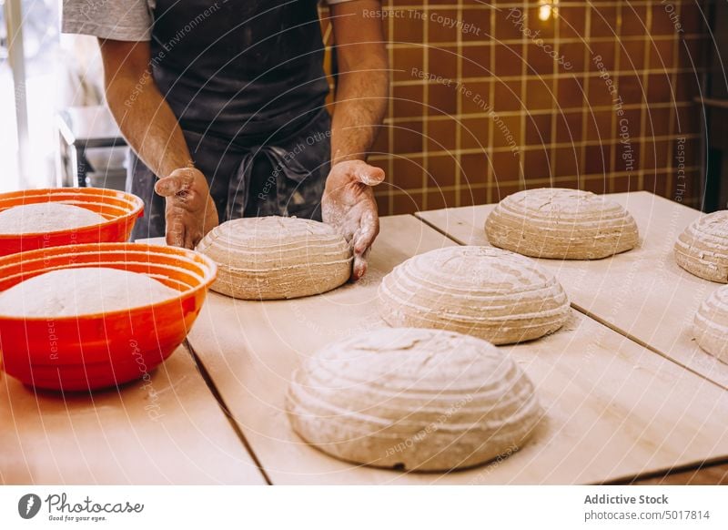 Männlicher Koch, der Teig mit einem Gärkorb formt Teigwaren vorbereiten Mann Bäcker Bäckerei roh Brot Form männlich Schürze hölzern Tisch Herstellung Prozess