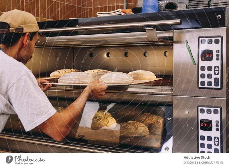 Mann beim Brotbacken im Backofen Bäckerei Ofen Koch Küche Teigwaren industriell männlich Tablett Schürze Gebäck vorbereiten Lebensmittel frisch kulinarisch