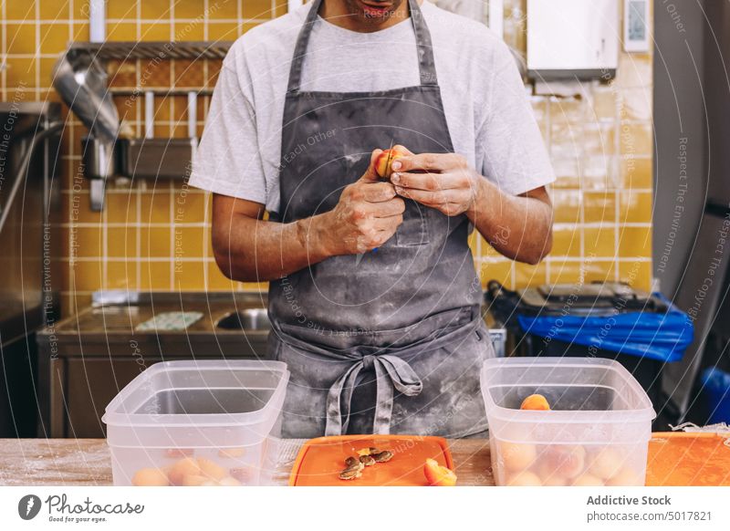 Crop männlicher Koch mit Nektarinenscheiben in der Küche Bäcker Frucht Bäckerei Pfirsich Mann vorbereiten dreckig Schürze frisch Lebensmittel roh professionell