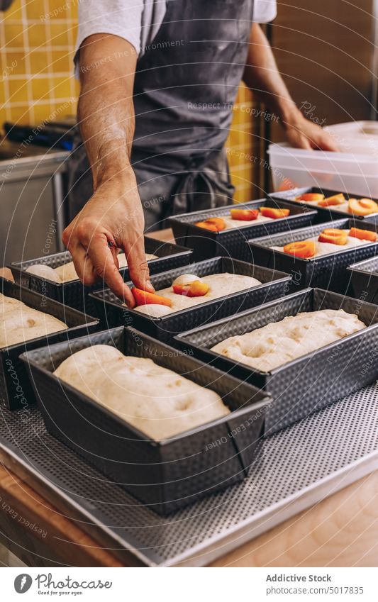 Männlicher Koch, der Früchte in den Teig gibt Gebäck Frucht Bäcker Pfirsich Mann hinzufügen Teigwaren roh frisch Bäckerei Speise männlich Schürze Lebensmittel