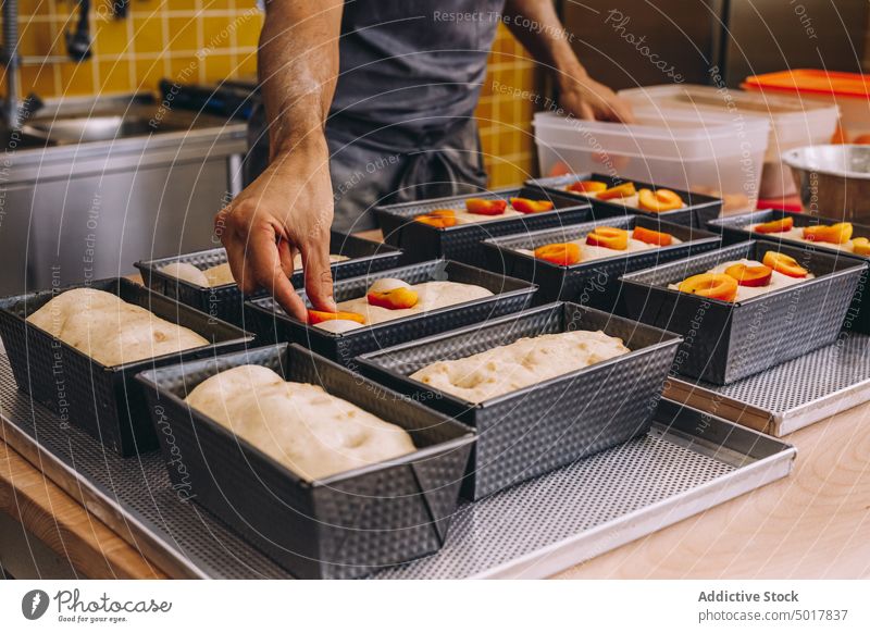 Männlicher Koch, der Früchte in den Teig gibt Gebäck Frucht Bäcker Pfirsich Mann hinzufügen Teigwaren roh frisch Bäckerei Speise männlich Schürze Lebensmittel