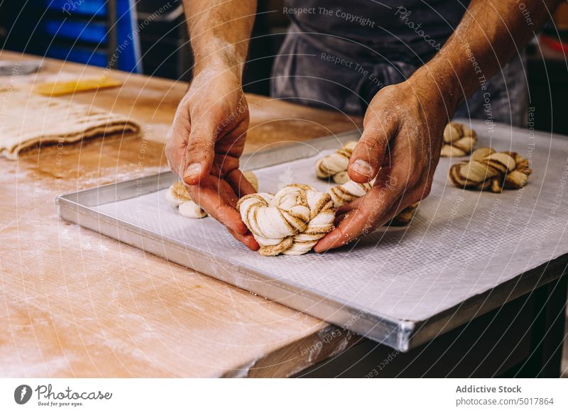 Männlicher Bäcker beim Backen von Zimtschnecken Teigwaren vorbereiten Mann rollen Brötchen roh ungekocht Form Prozess männlich Koch Bäckerei Mehl Tisch hölzern