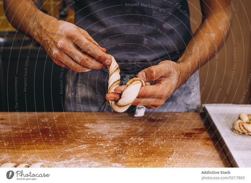 Männlicher Bäcker beim Backen von Zimtschnecken Teigwaren vorbereiten Mann rollen Brötchen roh ungekocht Form Prozess männlich Koch Bäckerei Mehl Tisch hölzern