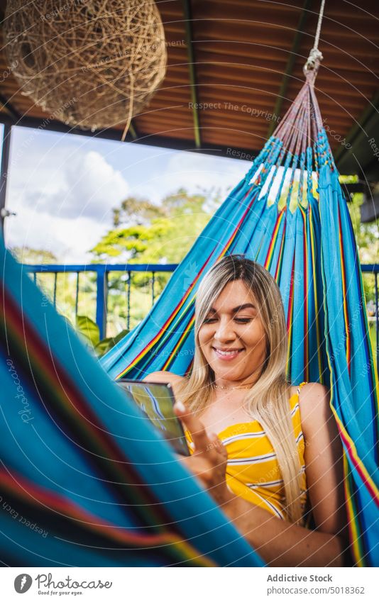 Lächelnde Frau, die auf ihrem Smartphone surft und sich in der Hängematte ausruht benutzend Kälte Zahnfarbenes Lächeln heiter Terrasse Resort