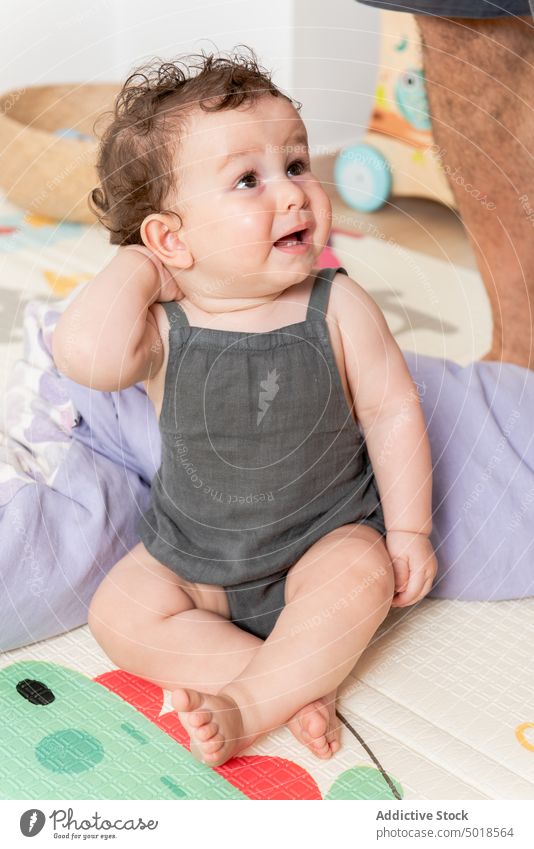 Entzückendes barfuß sitzendes Baby auf weicher Matte zu Hause neugierig bezaubernd spielen Unterlage heimwärts spielerisch Interesse Freude süß gemütlich ruhig