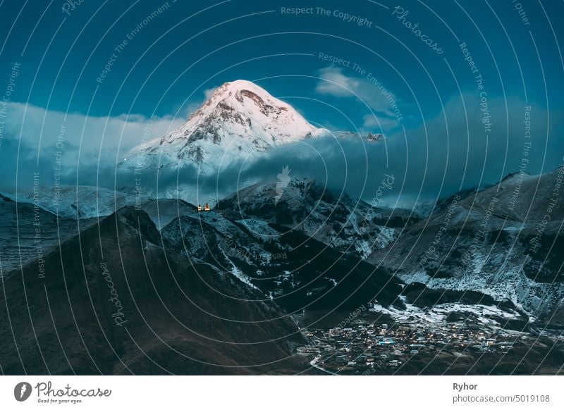 Stepantsminda, Georgien. Peak of Mount Kazbek mit Schnee bedeckt und berühmte Gergeti Kirche in der Nacht Lightning. Schöne georgische Landschaft im frühen Winter