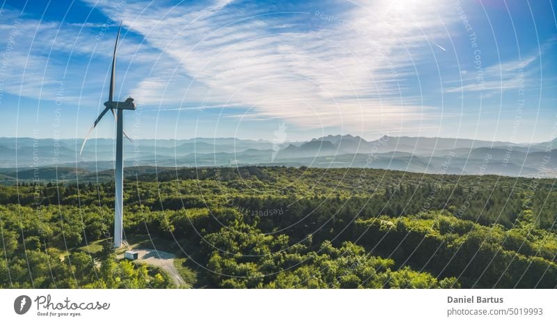 Blick auf einen Windpark in einem bergigen Waldgebiet mit Bergen im Hintergrund. Blick bei aufgehender Sonne. Sonnenaufgang. alternativ blau elektrisch