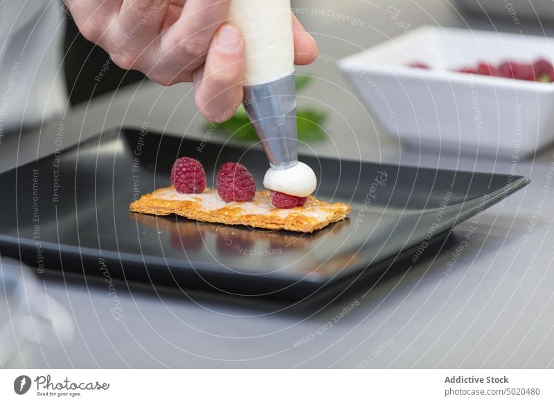 Professioneller Koch bei der Zubereitung eines Desserts mit Beeren und Zuckerguss Küchenchef professionell Spritzbeutel Speise ausgefallen Teller Himbeeren