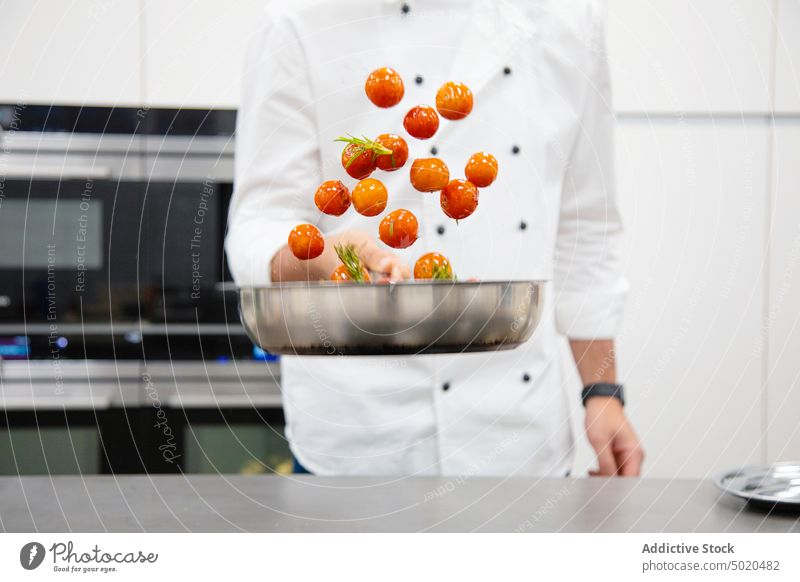 Profikoch beim Kochen und Schwenken von Kirschtomaten mit Kräutern Küchenchef Essen zubereiten werfend professionell Gewürz Kraut Pfanne Mischen führen Mann