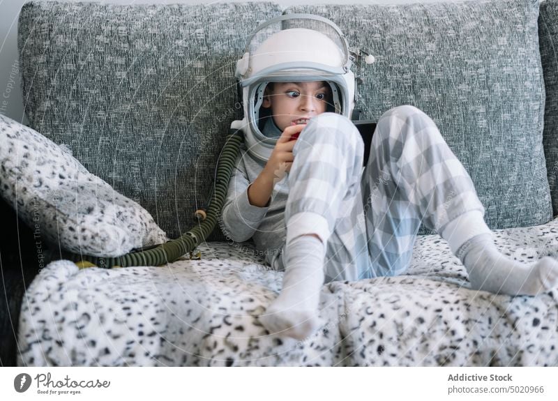 Kind liegt auf der Couch und spielt mit einer Videospielkonsole zu Hause Astronaut Hintergrund Junge Kindheit Konzept Tracht Schaffung handgefertigt Schutzhelm