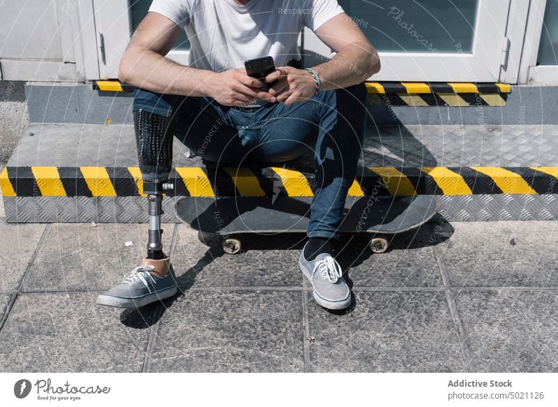 Crop Skater mit Beinprothese nutzt Smartphone Mann Skateboard künstlich Straße benutzend Großstadt jung urban männlich Prothesen modern Technik & Technologie