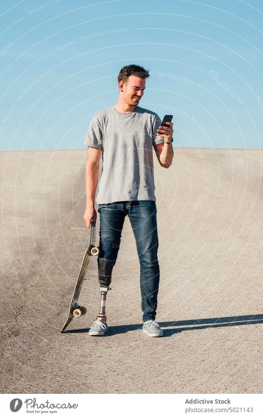 Crop Skater mit Beinprothese nutzt Smartphone Straße Skateboard Mann urban jung Großstadt im Freien Amputierte anonym künstlich Pause Browsen lässig Ernte