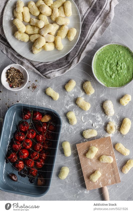 Rohe Gnocchi in der Nähe von Kochzutaten und Werkzeugen Teigwaren Kartoffel Tisch Küche Paprika Mehl Holzplatte Spätzle Teller gerippt vorbereiten Lebensmittel