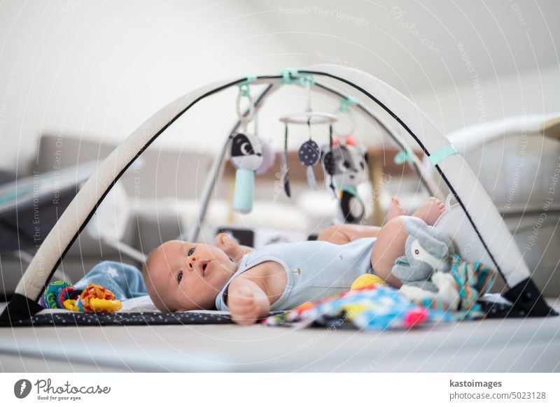 Niedliches Baby spielt mit hängenden Spielzeugen Bogen auf Matte zu Hause Baby-Aktivität und spielen Zentrum für frühe kindliche Entwicklung. Baby spielt zu Hause