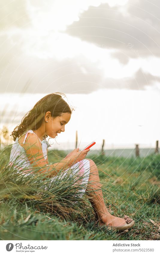 Hispanisches Mädchen beim Surfen auf dem Smartphone in einem Feld Sonnenuntergang Browsen Glück ruhen Wochenende Gras Sommer heiter Freude positiv Landschaft