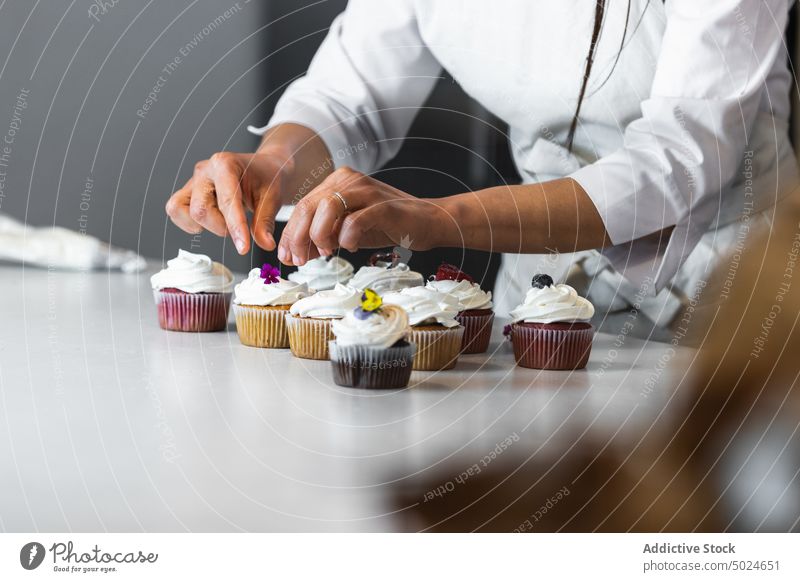 Crop Frau dekoriert Cupcakes auf dem Tisch in der Küche dekorieren Bäcker Bäckerei Küchenchef Koch Dessert Veganer Gebäck Gesundheit geschmackvoll kulinarisch