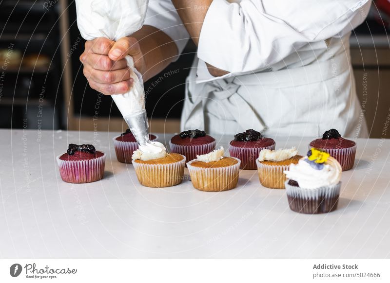 Crop Cook dekoriert Cupcakes mit Schlagsahne Bäcker gepeitscht Sahne drücken Backwarenbeutel Bäckerei Veganer Dessert Koch süß Leckerbissen gebacken