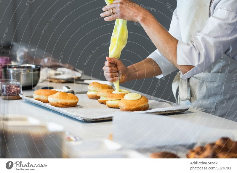 Kropfenkoch beim Verzieren von Berlinern mit Sahne in der Küche Bäcker berliner Backwarenbeutel dekorieren Dessert Koch vorbereiten Veganer süß Gebäck Bäckerei