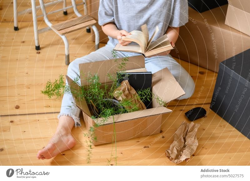 Anonyme Frau prüft Bücher in der Nähe von Kartons Buch prüfen Kasten Stock verlegen Flip Page heimwärts neu Appartement flach auspacken heimisch lesen