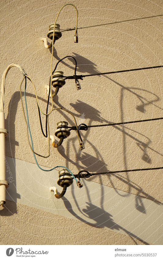 Vier Strom Isolatoren mit angeschlossenen Freileitungen an einer Hauswand, Schatten werfend Stromisolatoren Porzellanisolatoren Stromleitung Schattenspiel