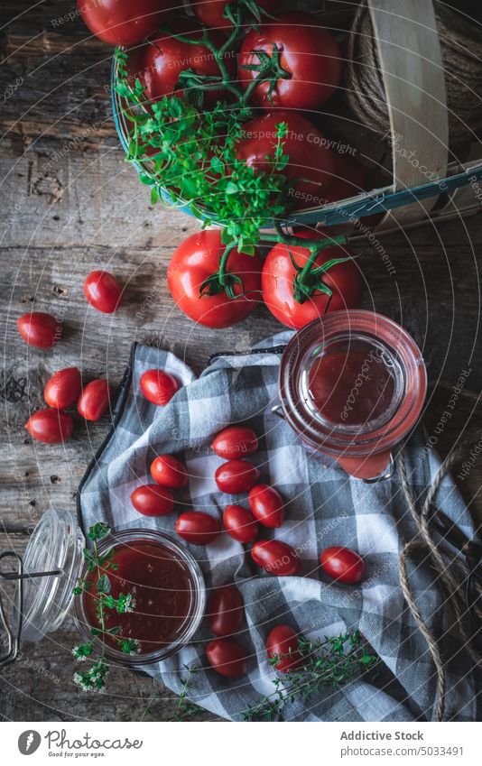 Tomaten und Kräuter neben Gläsern mit Marmelade Kraut Tisch Korb Serviette rustikal frisch Glas Zusammensetzung Küche reif Lebensmittel organisch Bestandteil