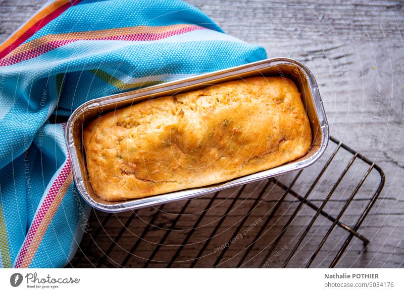 Hausgemachter Kuchen in einer Form auf einem Grill mit einem blauen Küchentuch Dessert Torte backen Backwaren Gebäck Rezept golden lecker Holztisch hausgemacht