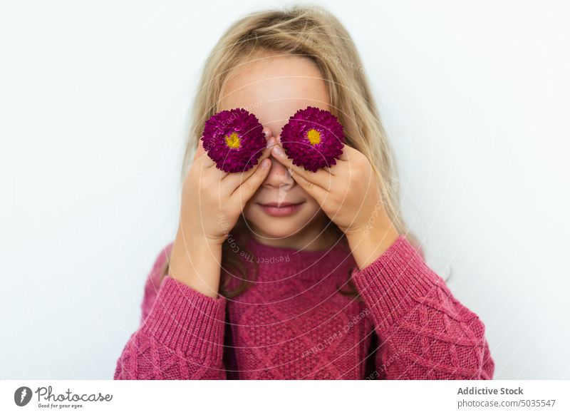 Mädchen bedeckt Augen mit blühenden Blumen Porträt Lächeln Kind Augen abdecken positiv Blütezeit Pullover purpur blond Glück heiter froh Freude schüchtern warm