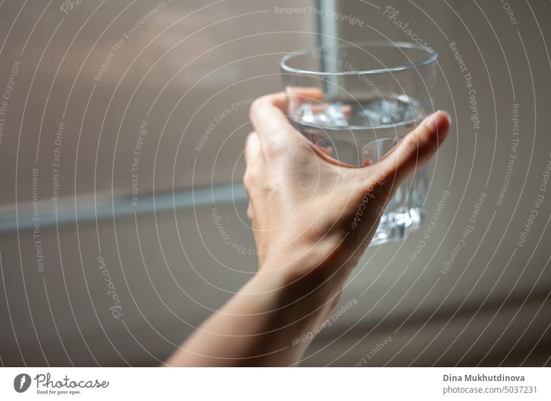 Morgens bei natürlichem Licht ein Glas Wasser in der Hand halten, in der Küche in der Nähe des Fensters. Hydratisiert bleiben. Ausreichend Wasser trinken. Gesunder Lebensstil. Hat einen Kater nach einer Party und trinkt Wasser. Weibliche Hand hält ein Glas Wasser.