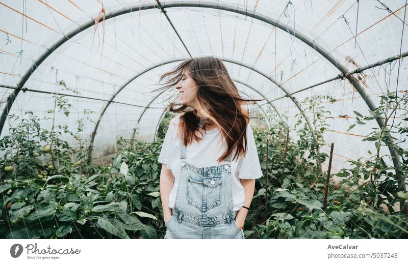 Frau bewegt Haare in der Mitte eines Gewächshauses stehend während der Arbeit.Gemüse neue Arbeit Konzept Landwirt Person Ernte Gartenarbeit Ernten 20s