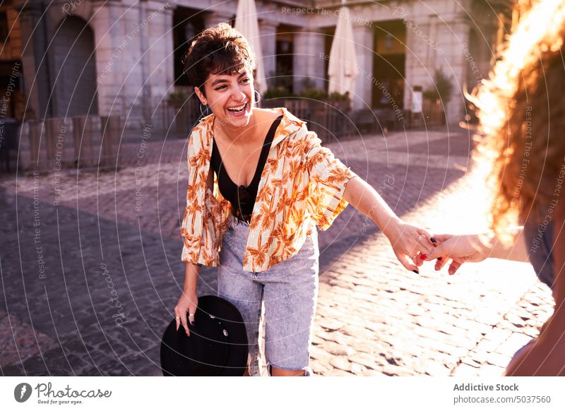 Glückliche Frauen halten sich auf einem sonnenbeschienenen Platz an den Händen Paar Händchenhalten Lachen Liebe Quadrat romantisch Wochenende Zusammensein