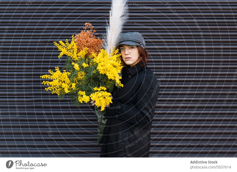 Frau mit Blumenstrauß vor grauer Wand Straße Oberbekleidung frisch urban Stil Herbst jung Blüte Verschlussdeckel Mantel Brille tagsüber Blütezeit Saison Haufen