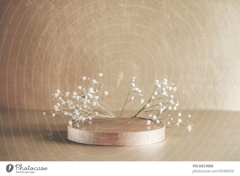 Beigefarbenes Produktdisplay mit Podest und kleinen weißen Gypsophila-Blüten. Szene Bühnenvitrine. Frontansicht mit Kopierfläche. beige Produktpräsentation